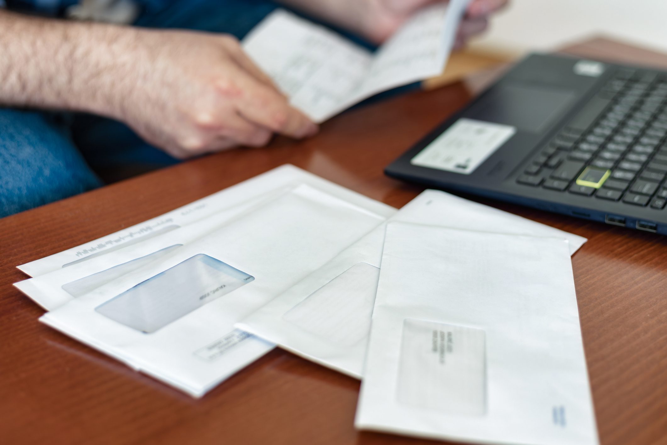 Man opening tax documents that came in the mail next to laptop