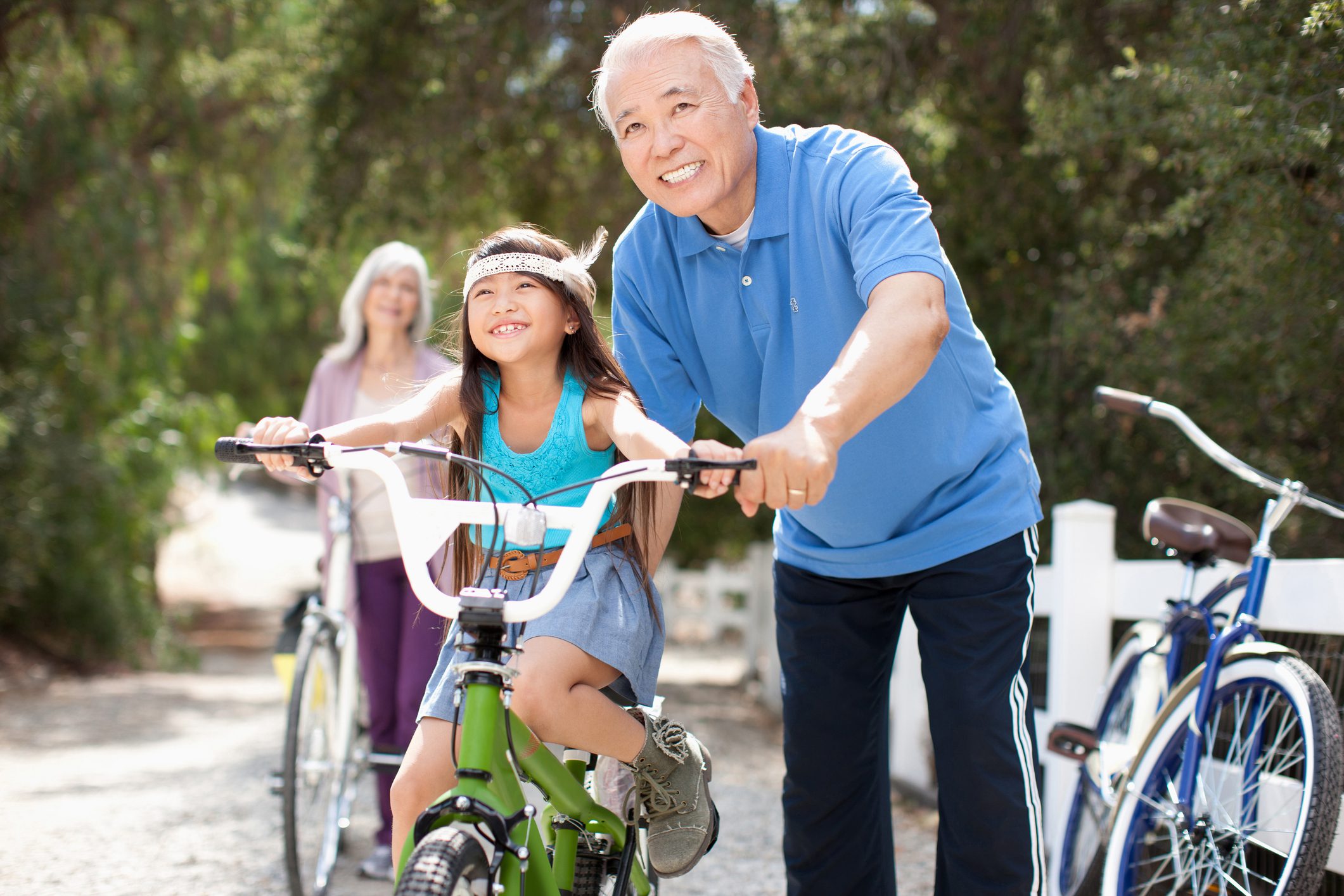 Grandfather helping grandaughter ride bike while contemplating how to help her achieve future financial success