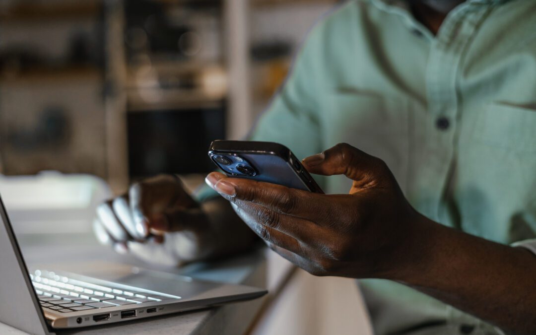 Hand holding cell phone next to laptop for two factor password authentication