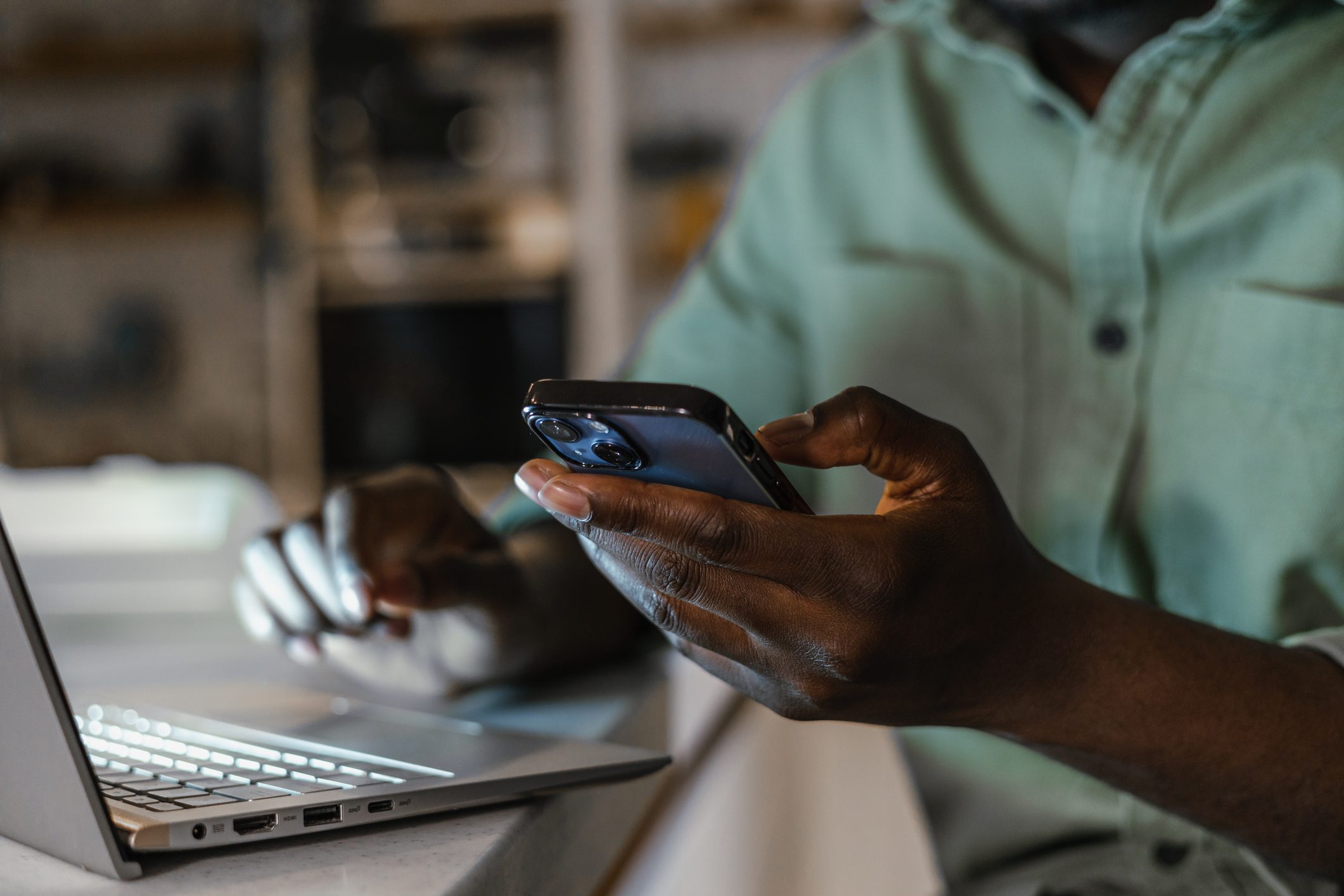 Hand holding cell phone next to laptop for two factor password authentication