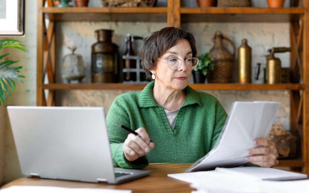 A woman who has her glasses on and is looking at tax documents and her laptop to consider tax saving strategies