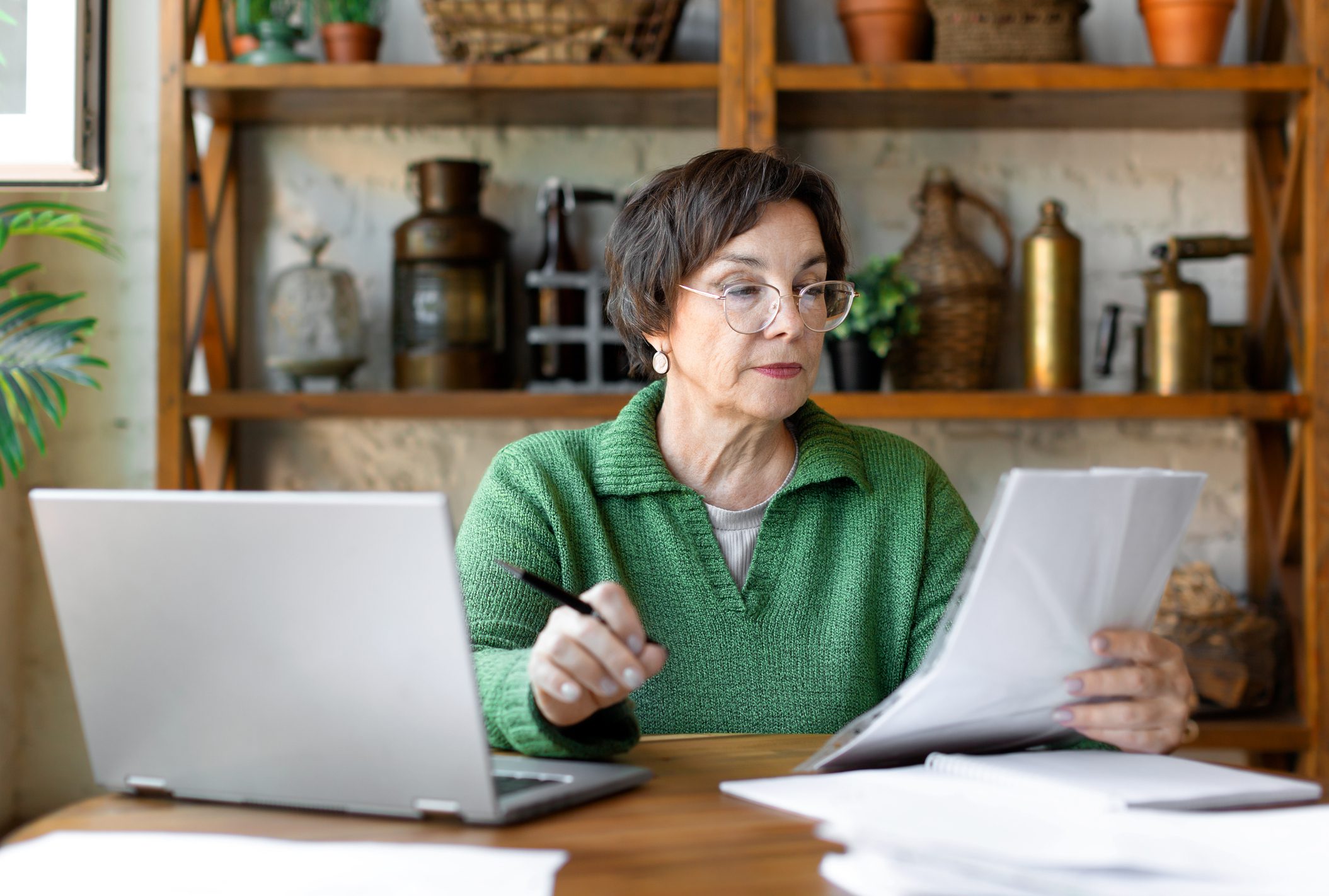 A woman who has her glasses on and is looking at tax documents and her laptop to consider tax saving strategies