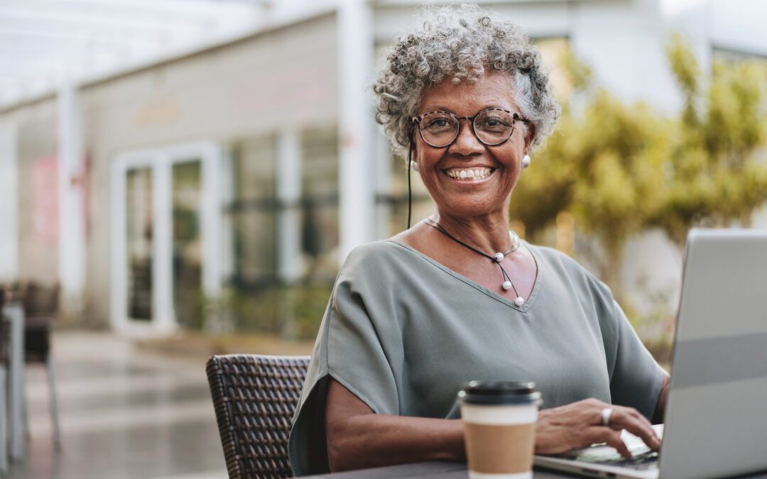 Senior woman returning to work after retirement adn working on laptop next to to-go cup of coffee