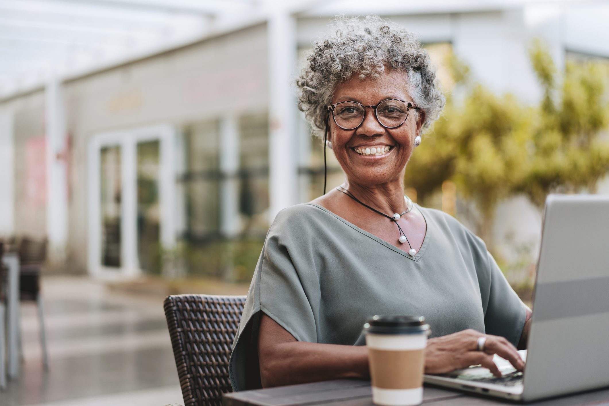 Senior woman returning to work after retirement adn working on laptop next to to-go cup of coffee